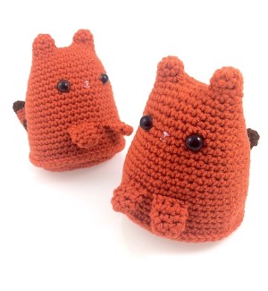 Two orange cone shaped crochet tigers with pointy ears, flat hands and a striped tail.