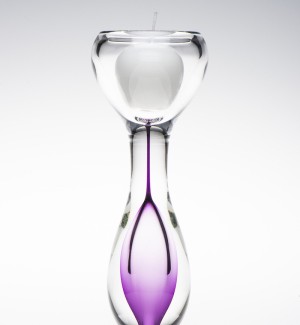 An hourglass shaped clear glass candle holder with purple inside the bottom of the hourglass shape.
