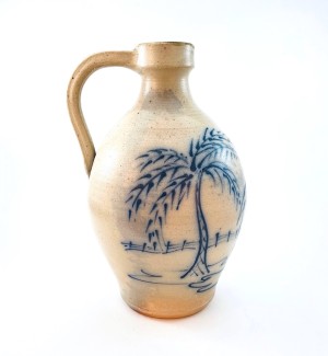 A cream colored ceramic jug with a blue illustration of a palm tree and deer on the front.
