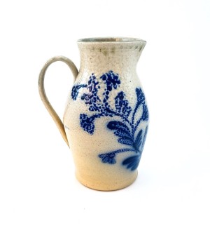 A white ceramic pitcher with a blue illustration of a vine across the front.