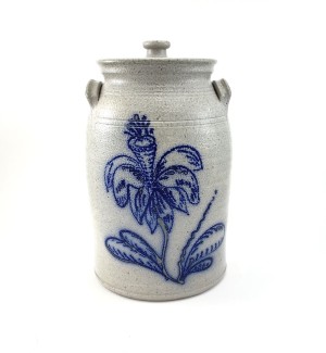 A cream colored ceramic lidded jar with a blue illustration of a trumpet flower on the front.