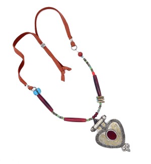 a necklace made partly with a cord and partly with a colorful assortment of different shaped beads and a metal pendant with decorative elements shaped like a heart with a red stone in the center.