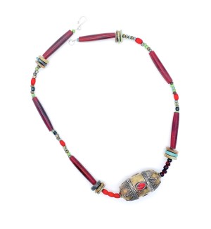 a necklace made with a colorful assortment of different shaped beads and a metal pendant with decorative elements shaped like a capsule with a red stone in the center.