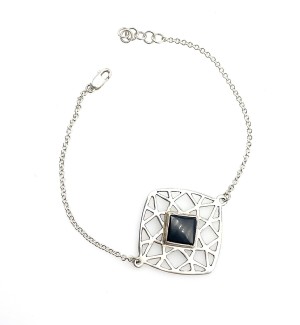 A bracelet with a large carved geometric pattern with a square gemstone in the center.