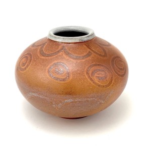 Round rust orange vessel with arcing and spiral patterns and a white rim.