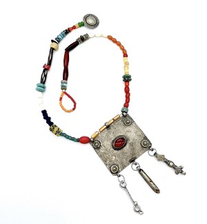 a necklace made with a colorful assortment of different shaped beads and a square metal pendant with dangling elements and a red stone in the center.