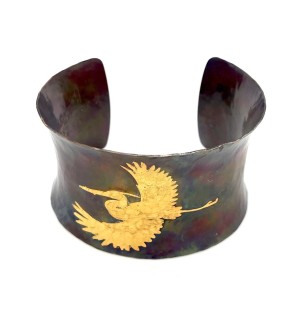 A wide copper cuff bracelet with a gold illustration of a heron in flight.