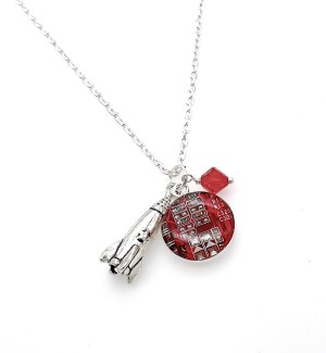 A red pendant with a circuit board design and silver rocket charm and red diamond shaped bead on a silver chain.