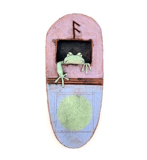 A hanging, oval shaped ceramic wall tile with a green frogs head and arm sticking out. 