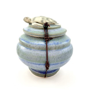 Blue ceramic lidded pot with a sea turtle on the lid and a waxed leather cord tied around it.