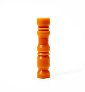 Tall and narrrow terracotta colored candle with angled cuts in surface.