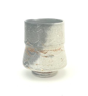 Ceramic tiered cup with a wave pattern over a subtle, mottled and pebbled surface in light grey with a sharp diagonal shift to a dark grey background. 