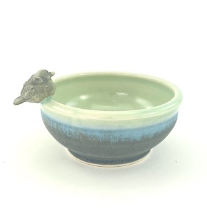 A low shallow ceramic bowl with a bird perched on the rim. The glaze blends from a moss green at the base to a ribbon of bright blue to celedon green on the lip and interior.