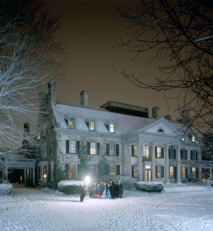 a color photograph of a Greek Revival architectural house in white granite with a collanade on the front with a dark amber sky and snow on the lawn.