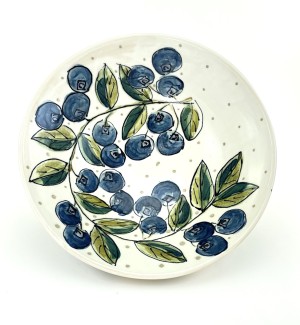 White ceramic bowl with hand illustrated blueberries and a garland of green leaves arranged around the interior perimeter.