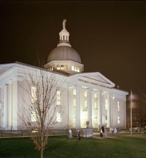 a panoramic nighttime view of a white granite classic Greek Revival style building with columns and a large rounded dome on the roof.