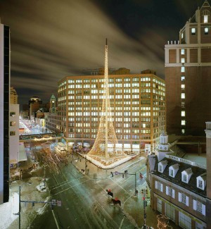 a nightime city street scape with an Eiffel tower like sculpture strung with white lights in a central plaza with a multi story brick building in the background.