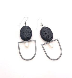 a pair of earrings with a textured black oval stone over a silver U-shaped form with a white pearl within.