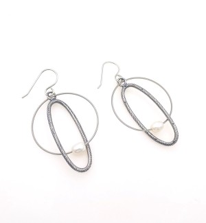 a pair of earrings with a round silver hoop and an oval hoop that look like a mobile with a white pearl bead.