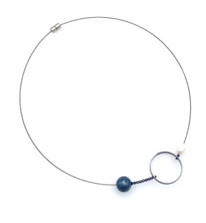 a necklace made of a single steel cable strung with a single white pearl, Sterling silver circle, small faceted gemstones and a metal ball with a magnetic closure.