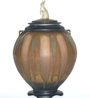 a large scale ceramic jar with a decorative base and a white rabbit standing on the lid.