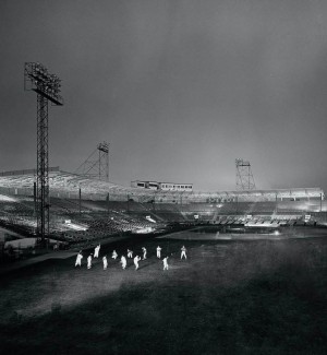 a black and white photograph of a nightime baseball game inside a circular sadium.