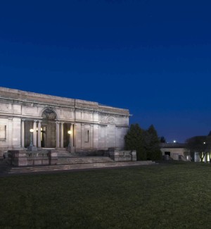 a panoramic color photograph of two granite buildings on grassy grounds with a deep blue nightime sky.