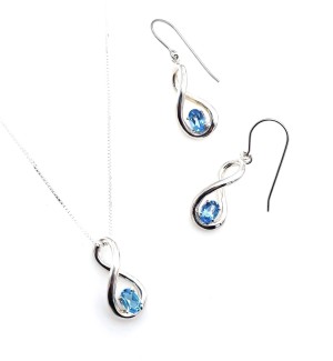 A pair of silver earrings shaped like infinity symbols with a blue gemstoneperched in the center placed next to a necklace with the same infinity design.