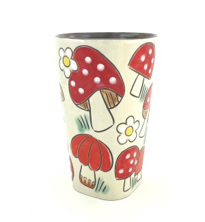 a ceramic tumbler with a white background and large red capped, white polka dotted mushrooms.