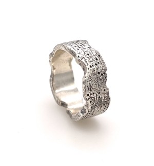 a wide band silver ring with an uneven edge and carved symbols on the surface.