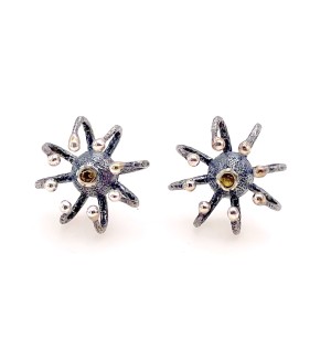 a sculptural earrings with a protruding eight legged spider form with a yellow stone in the center.
