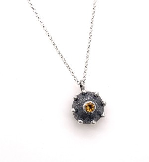 a handmade pendant made of silver in a dome shape with a yellow stone in the center.