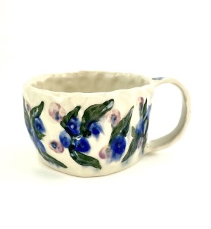 a hand formed ceramic mug with hand illustrated blueberries and green leaves.