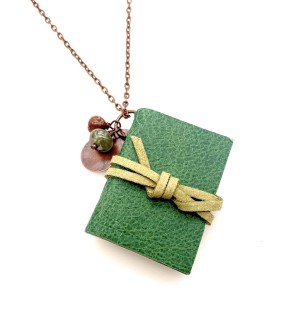 A mini green hand bound book with a light green cord on a long copper tone chain with two small beads.