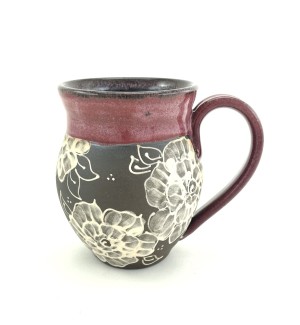 a ceramic mug with dark clay body illustrated with roses and glazed in a rose hued glaze at the rim and handle.