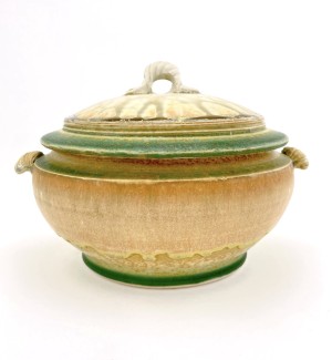 a round, lidded ceramic casserole dish with a pumpkin colored glaze with green rims on the lid.