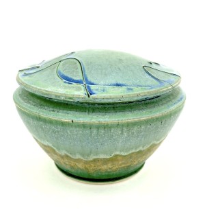 a round ceramic lidded dish with a green glaze and a drizzle of blue decoration on the lid.