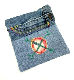 a zipper pouch made of blue jean material with a hand painted and embroidered circular patch.