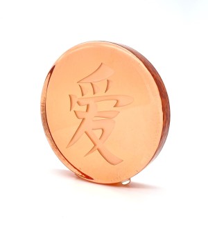 a round peach colored transluscent glass disc etched with a Chinese charature meaning 'Love'.