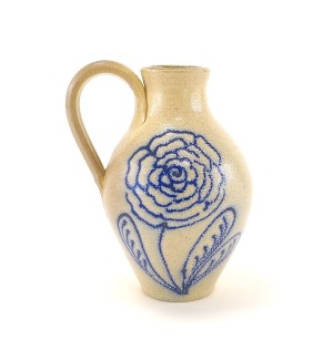 a ceramic jug with a loop handle, a pebbly glazed oatmeal colored body with a hand illustrated flower in blue.