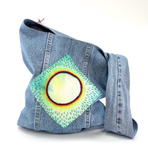 a handsewn blue jean fabric shoulder bag with a hand painted and embroidered design that resembles a full eclipse of the sun..