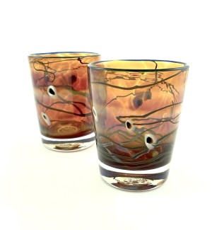 a set of hand blown whiskey glasses with a golden glass body accentuated with striations of white and blue with a bright blue glass edge.