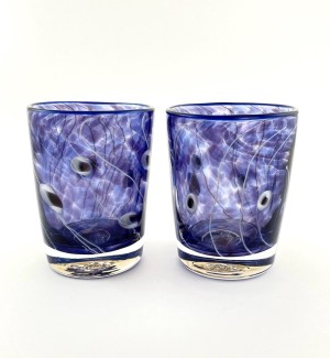 a pair of hand blown glass whiskey glasses with a clear and purple striation pattern.