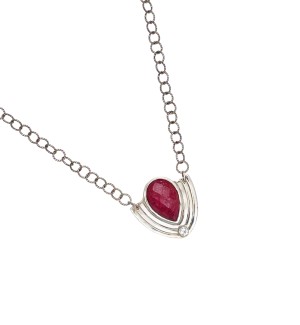 a pendant with a faceted teardrop pink tourmaline bezel set in Sterling silver. Accentuated with a pop of shine from a topaz and boldly framed with a shape reminiscent of a shield.