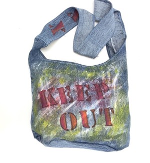 a handsewn shoulder bag of blue jean material with a painted illustration of stenciled letters 'Keep Out'.