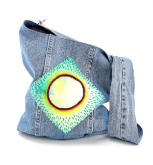 a handsewn blue jean fabric shoulder bag with a hand painted and embroidered design that resembles a full eclipse of the sun. 