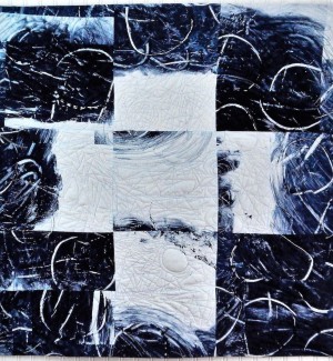 a painterly fabric quilt with an overriding nine box grid that resembles a tic tac toe board in blues and whites.