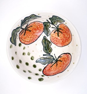 a white ceramic bowl with hand illustrated red tomatoes and green leaves arranged around the interior perimeter.