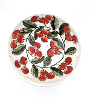 a white ceramic bowl with illustrations of red cherries, green leaves and a moth with wings.