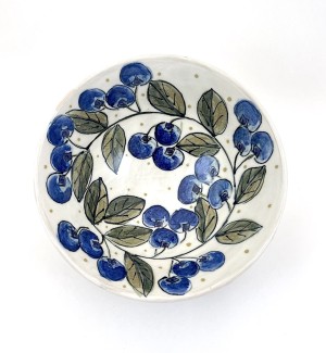 a white ceramic bowl with hand illustrated blueberries and a garland of green leaves arranged around the interior perimeter.